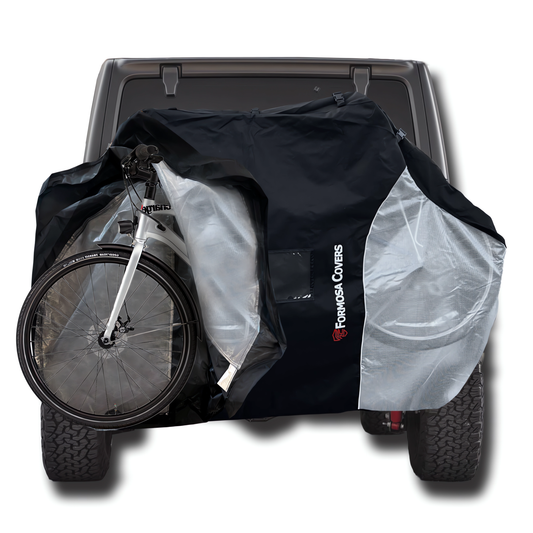 A black and white bicycle mounted on the back of a vehicle is partially covered by Formosa Covers' heavy-duty, black and silver Cosmetic Defect - Quad Bike Rack Cover For Transport (Fits 3-4 Bikes) Extra Large Translucent Ends. The cover is designed to shield the bike from elements, offering UV protection during transportation.