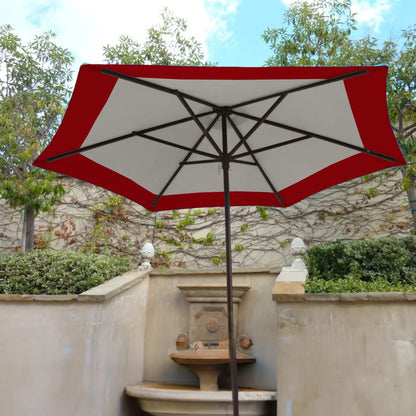 A 9ft Market Patio Umbrella 6 Rib Replacement Canopy Duet Red by Formosa Covers, made from 300 denier polyester fabric, is open, providing shade over a garden area with a stone water fountain. The backdrop features a light-colored, vine-covered wall and lush greenery, with a partly cloudy sky above.