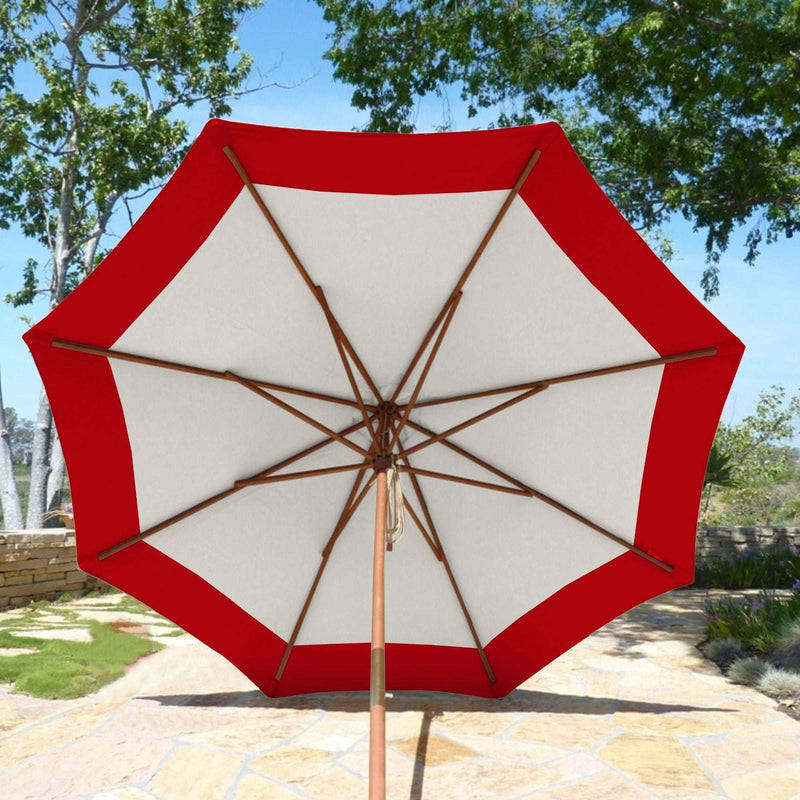 The 9ft Market Patio Umbrella 8 Rib Replacement Canopy Duet Red by Formosa Covers is open against a backdrop of greenery and a stone walkway. The umbrella's wooden pole and ribs are visible, with trees in the background under a clear sky.