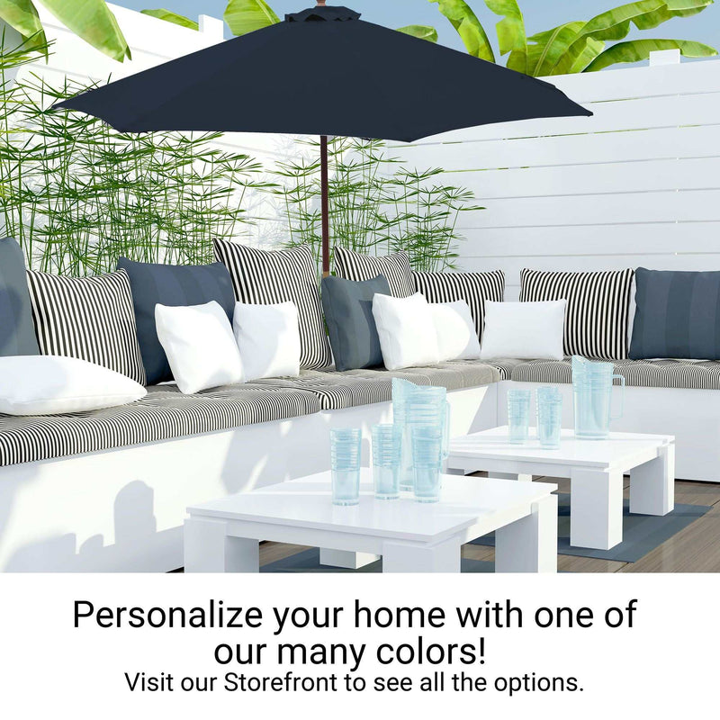 A modern outdoor patio setup featuring a cushioned L-shaped sofa adorned with striped and plain pillows, a large, durable 11ft Market Patio Umbrella with an 8 Rib Replacement Canopy in Dark Blue by Formosa Covers, and two white coffee tables with blue glassware on top. Lush green plants and a white fence provide a serene backdrop. Text reads: "Personalize your home with one of our many colors! Visit our Storefront to see all the options.