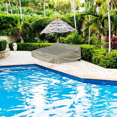 A serene backyard features a swimming pool bordered by lush greenery and stone pavers. Two lounge chairs, protected by the Patio Double Chaise Lounge Cover 84