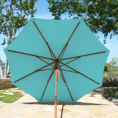 A 9ft Market Patio Umbrella with an 8-rib Glacier Blue canopy from Formosa Covers stands open on a stone-paved patio with trees and greenery in the background. Made from UV-treated, durable polyester fabric, the umbrella provides ample shade and a relaxing outdoor atmosphere.