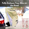 A black car is equipped with a hitch mount bike rack, covered by the Formosa Covers OPEN BOX - NEW COLOR Dual Bike Rack Cover for Transport, which fits 1-2 bicycles and features large translucent ends and a license plate holder. This heavy-duty poly cover in beige includes reflective panels and a transparent section, offering protection against water, debris, UV rays, and snow. In the background, three deer are seen standing near some trees.