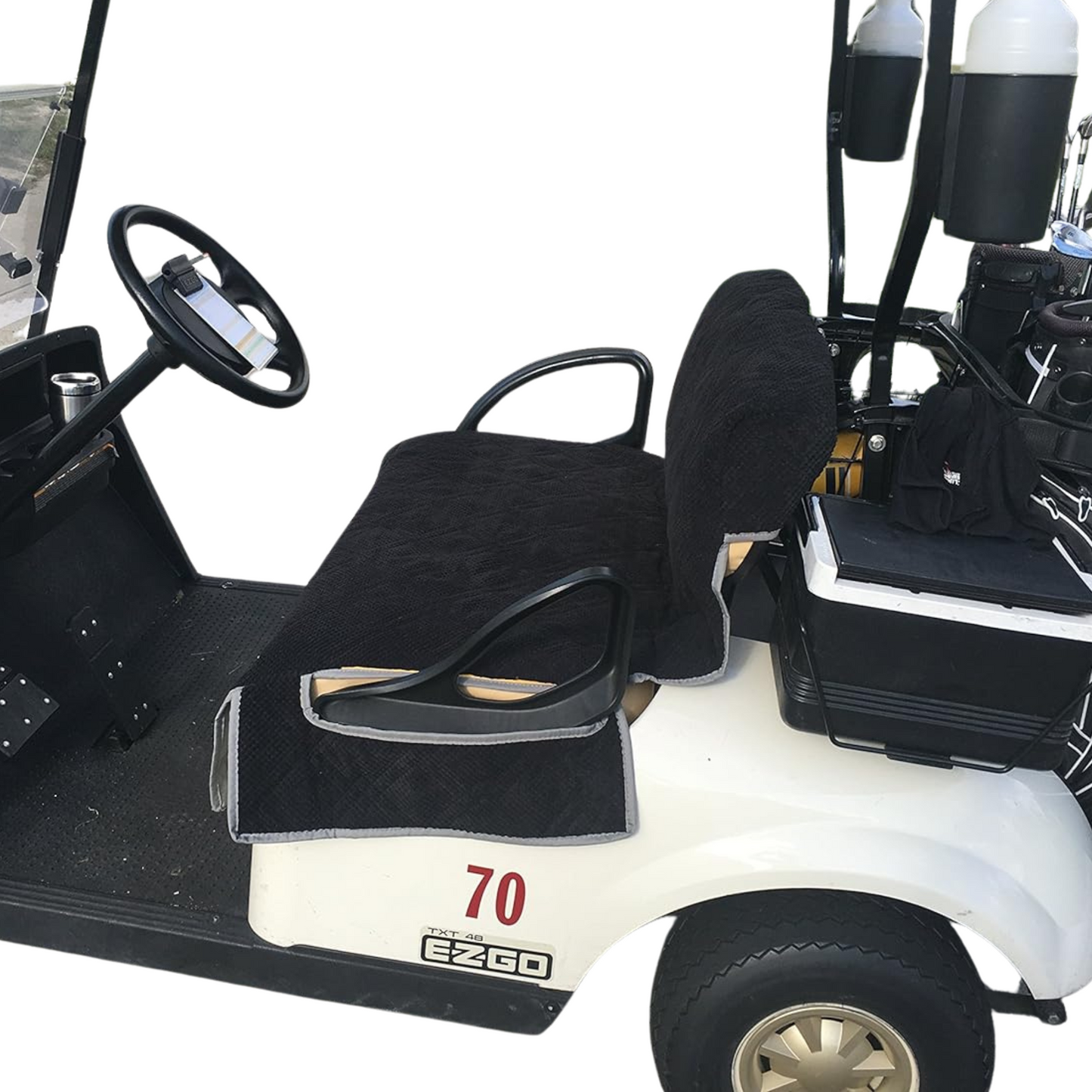 A white golf cart with a Formosa Covers Reversible Golf Cart Dual Seat Blanket Cover in black and taupe is parked, featuring the number 70. The dashboard includes a steering wheel, cup holder, and a mounted tablet. The back of the cart has additional seating and several hanging bags. Beige hubcaps enhance the wheels for added style.